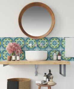 Round wooden-framed mirror above a white vessel sink with a turquoise patterned tile backsplash and bathroom counter items like bottles and brushes.