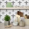 | Casadart | Vinis Autocolantes, Papel de Parede e Painéis Decorativos Shelf in a kitchen with glass jars of grains, a tall stack of green plates, cutting boards, a rolling pin, and a plant.