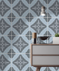 Interior scene with a blue-gray geometric tiled wall behind a wooden two-drawer sideboard, a small glass display, a potted plant, and a hanging pendant light above.