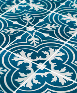 Close-up of blue ceramic tiles featuring a white scrolling floral pattern and visible grout lines forming an overlapping diagonal grid.