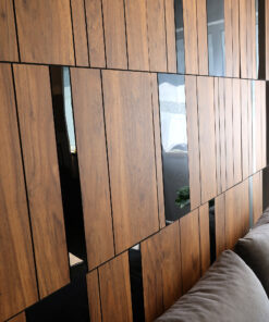 Interior wall clad in vertical wood slats with slim glass inserts; a gray sofa is visible in the foreground on the right side.