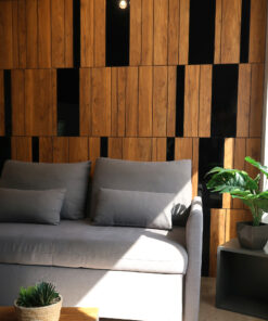 Gray upholstered sofa with multiple cushions against a warm wood-paneled wall in a modern living area, with a potted plant on a side table nearby.