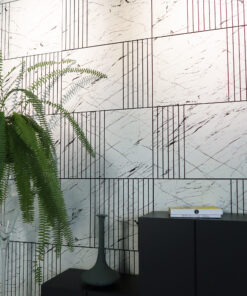 Green ferns sit beside a dark desk and modern lamp against a marble-patterned wall with a few stacked books on top of the cabinet.
