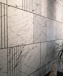 White marble wall divided into rectangular panels by black grid lines, with two white vases and a tall plant on the right.
