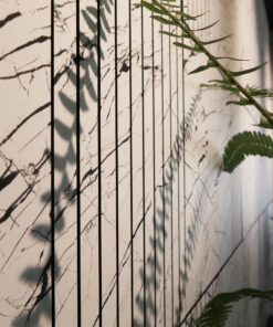 Indoor marble wall with black vertical slats and a green plant branch casting shadows in the foreground.