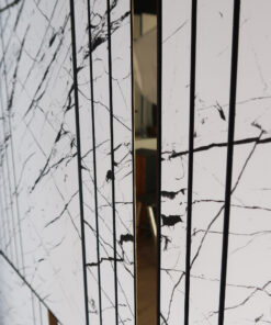 Close-up of a marble wall with dark vertical bars and a narrow gold-lined panel, showing a blurred interior reflection.