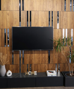 Modern living room wall with vertical wooden panels and mirrored inlays, mounted flat-screen TV center stage, plants on right, and decorative HOME letters on a dark console.
