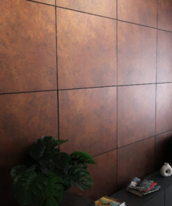 Rusty brown tiled wall with black grout lines, a large green plant in the foreground and shelves with magazines and a white sculpture on the right.