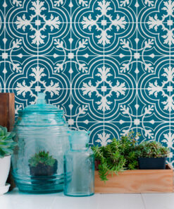 Arrangement of turquoise ceramic water jars and various succulents in front of a bold blue patterned tile wall, creating a decorative display.