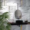 NS895-dourado-3 | Casadart | Vinis Autocolantes, Papel de Parede e Painéis Decorativos Modern bathroom wall with marble tiles, black grid lines, and gold vertical accents; circular concrete sink and black faucet visible with green plant in foreground.