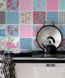 Stove with a metal kettle and a pan on a black cooktop against a colorful patchwork tile backsplash.