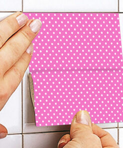 Close-up of hands folding a pink polka-dotted paper along a crease on a tiled surface.