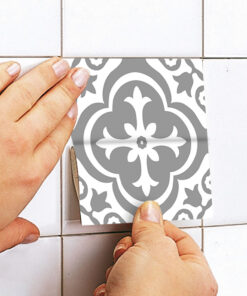 Close-up of hands applying a gray and white patterned tile sticker to a white tiled wall, aligning it with the grout lines.