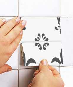 Hands place a white tile with a black floral pattern into a wall of plain white tiles (close-up).”,