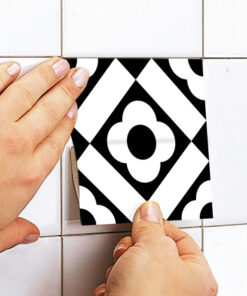 Close-up of hands installing a square black-and-white geometric patterned tile onto white wall tiles.