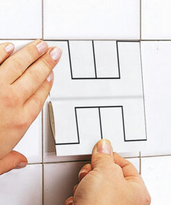 Close-up of hands placing a tile layout template on white wall tiles to plan a stepped pattern.