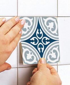 Person placing a blue and white ornamental tile sticker onto a white tiled wall, peeling from the back