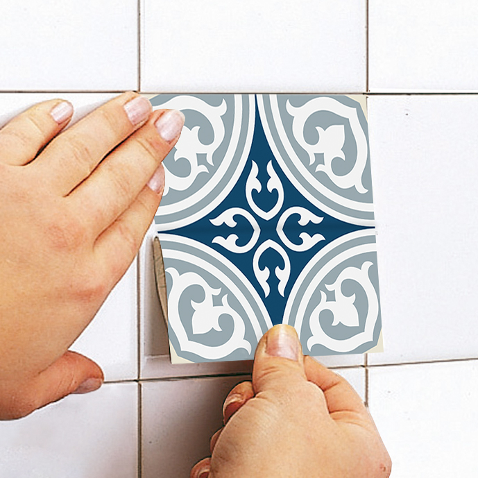 apply | Casadart | Vinis Autocolantes, Papel de Parede e Painéis Decorativos Person placing a blue and white ornamental tile sticker onto a white tiled wall, peeling from the back