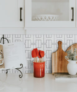 White kitchen scene featuring white cabinets with dark handles, a red utensil holder, an open cookbook, and wooden cutting boards on a counter.