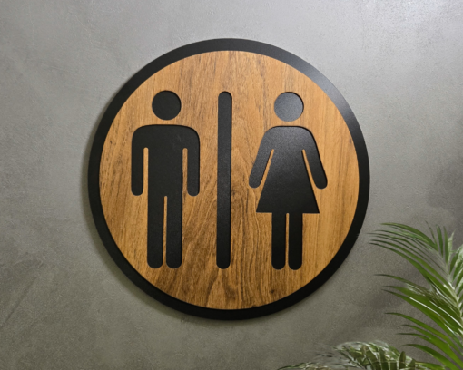 Circular wooden sign with black male and female restroom silhouettes on a gray wall.
