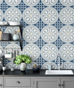 Grey kitchen counter with a blue geometric tiled wall; shelves hold cups, plates, kettle, toaster, and utensils; a green plant sits in a marble vase.