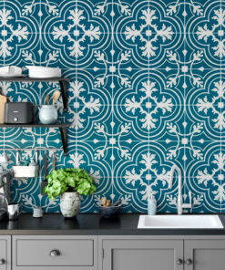 Kitchen with teal patterned tile backsplash, gray cabinets, a toaster and kettle, stacked dishes, and a green potted plant.