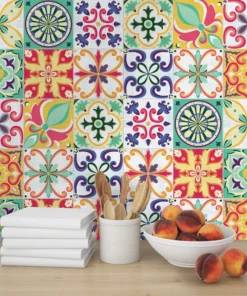 Colorful tile-patterned wall over a wooden countertop with a stack of white books, a utensil holder with wooden spoons, and a bowl of peaches.