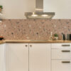 a kitchen with white cabinets and a sink and a | Casadart | Vinis Autocolantes, Papel de Parede e Painéis Decorativos Stainless steel range hood above white cabinets with a speckled terrazzo backsplash in a modern kitchen.