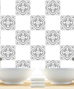 Double white ceramic sinks with chrome faucets above a wooden counter and patterned gray tile wall, towels in the center.