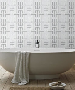 White freestanding bathtub with a towel draped over the side, in a bathroom with geometric tiled wall and wooden floor.