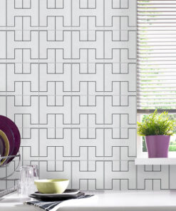 White kitchen wall with a bold black geometric tile pattern, stacked dishes on a rack to the left, and a window with blinds on the right.