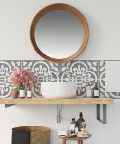 Round wooden-framed mirror above a white sink with patterned gray tile backsplash and assorted bottles on the counter area.
