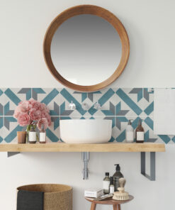 Round wooden-framed mirror above a white sink with a blue geometric-tile wall and pink peonies on a wooden shelf with toiletries nearby.
