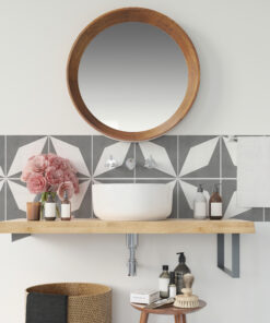 Round wooden-framed mirror above a bathroom sink with gray geometric tiles and pink flowers nearby in the scene.