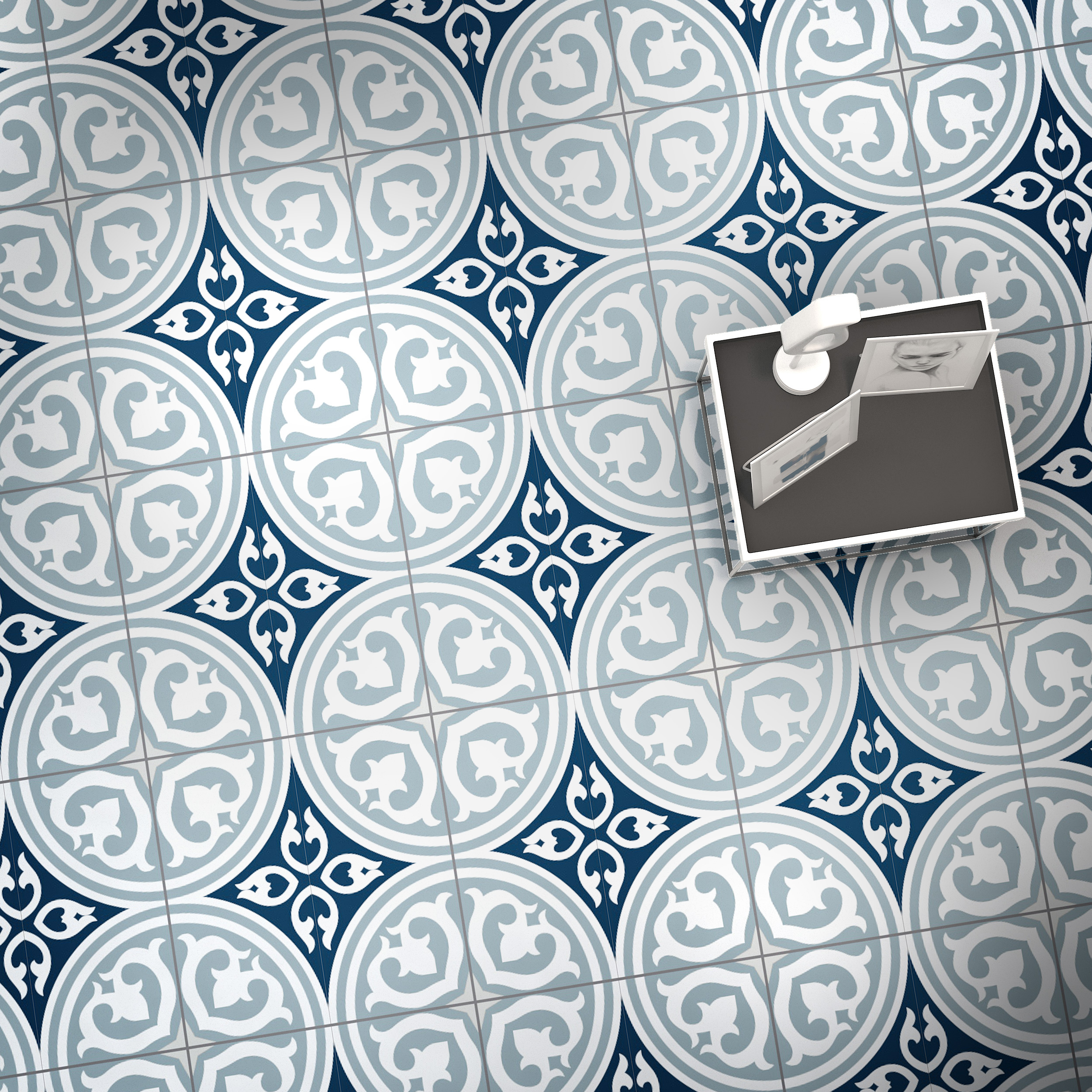 x550000 | Casadart | Vinis Autocolantes, Papel de Parede e Painéis Decorativos Top-down view of a tiled floor with blue and gray circular medallions; a desk with photos sits in the corner (decorative pattern).