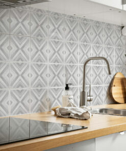 Gray geometric chevron tile backsplash behind a stainless steel sink and faucet on a wooden counter, with a soap dispenser nearby.
